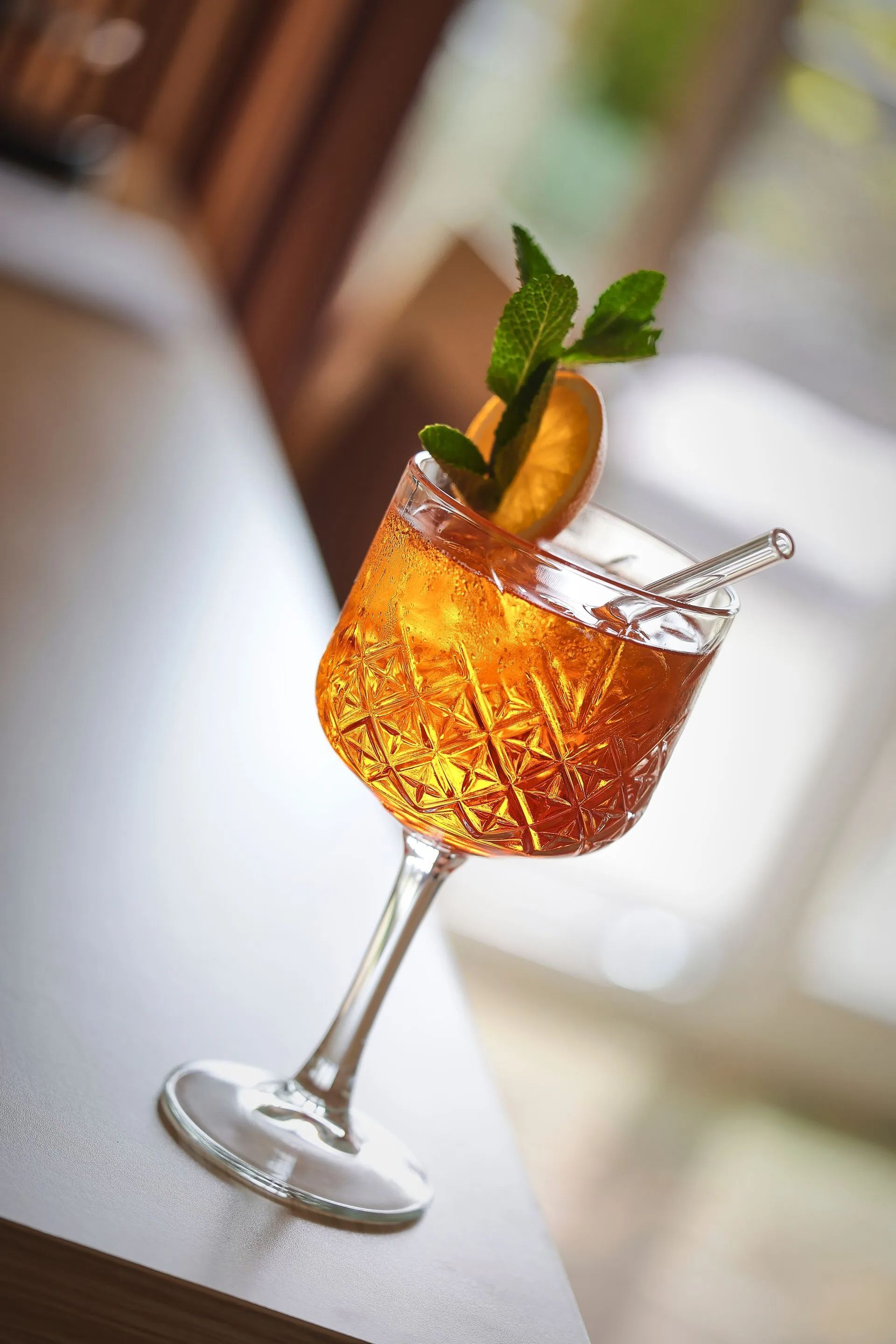 Cocktail im geätzten Glas, garniert mit Orangenscheibe und Minze, auf weißem Untergrund.