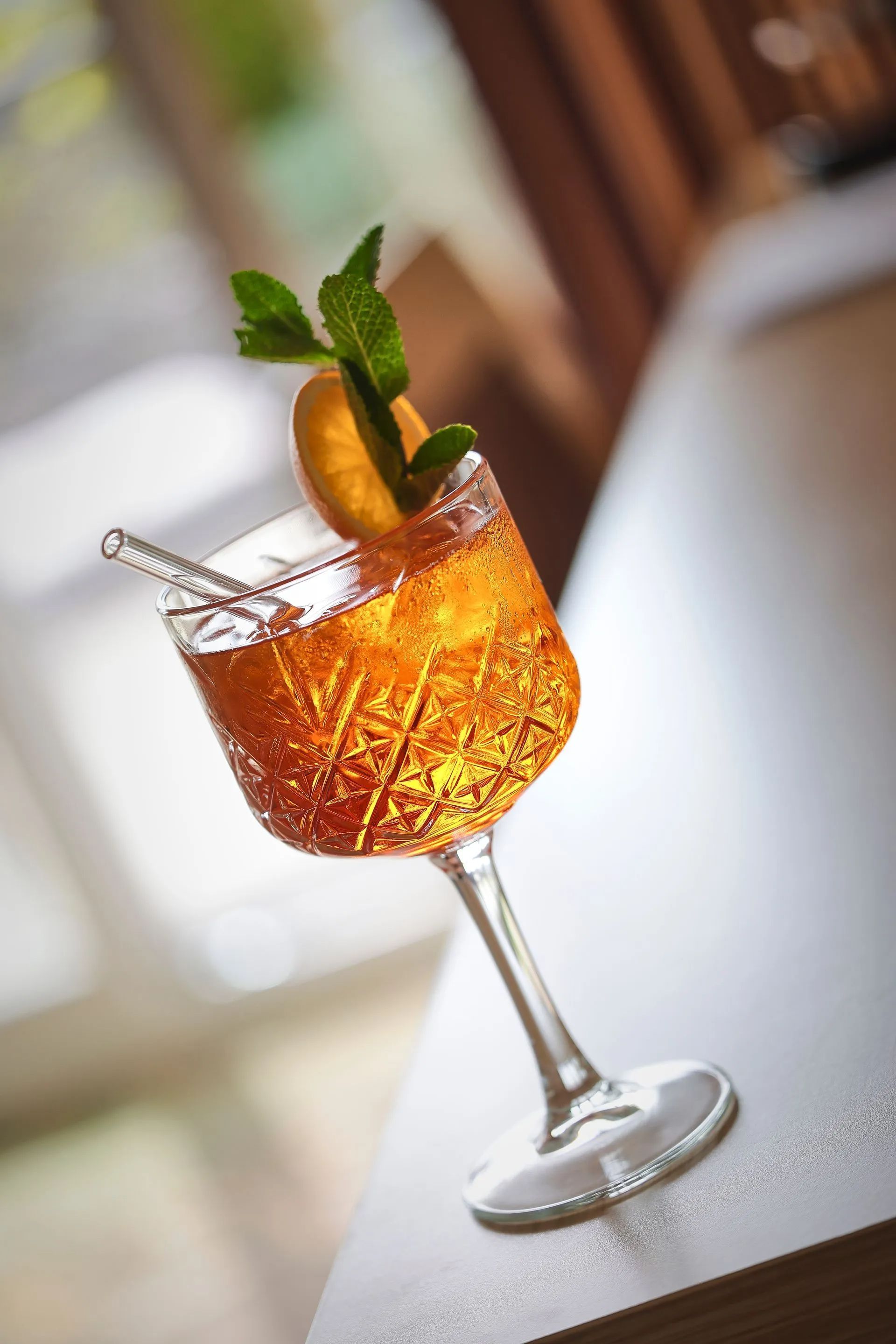 Cocktail in einem Stielglas, garniert mit Orangenscheibe und Minze, auf einem Tisch.