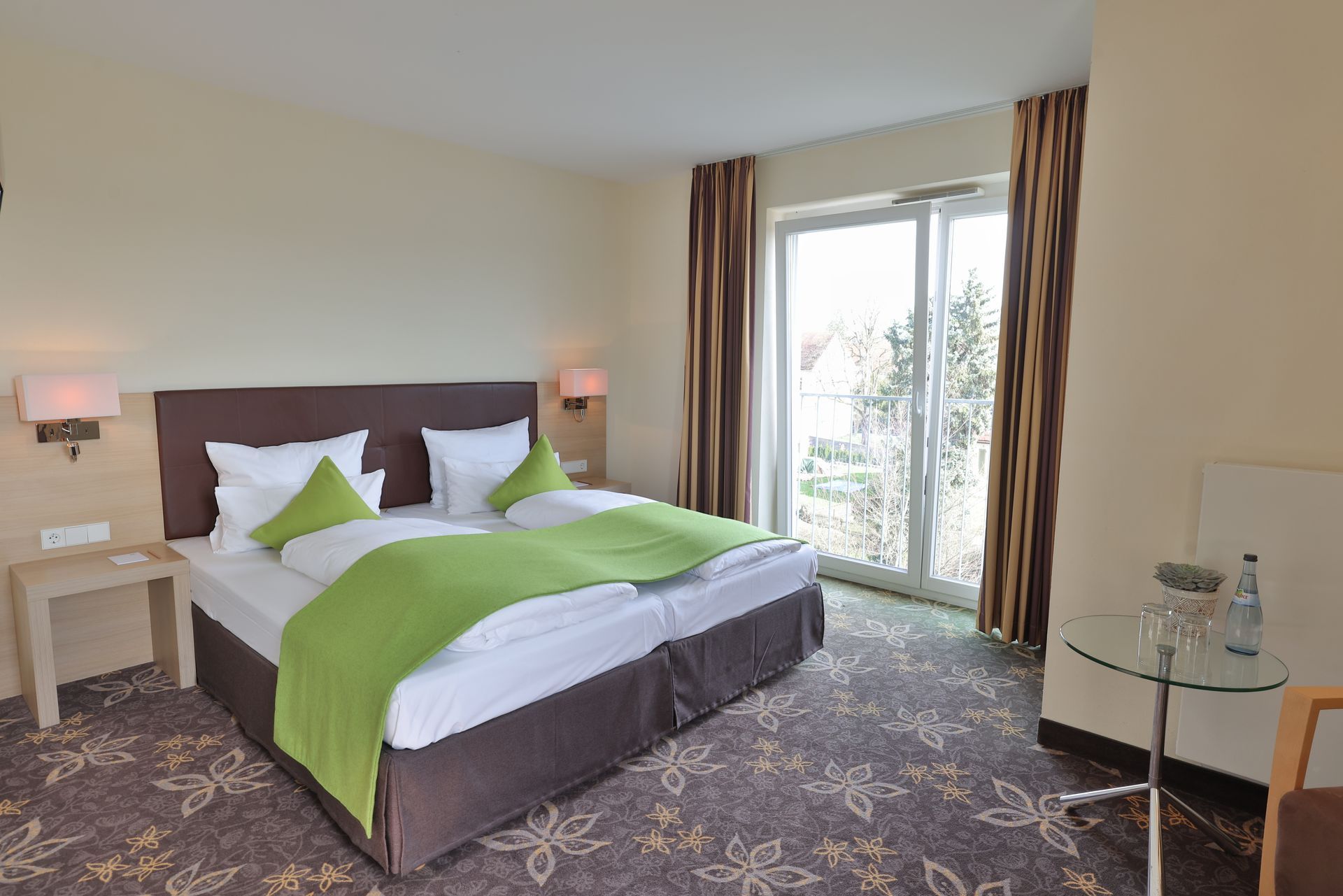 Hotelzimmer mit Doppelbett, lindgrüner Decke und großem Fenster.