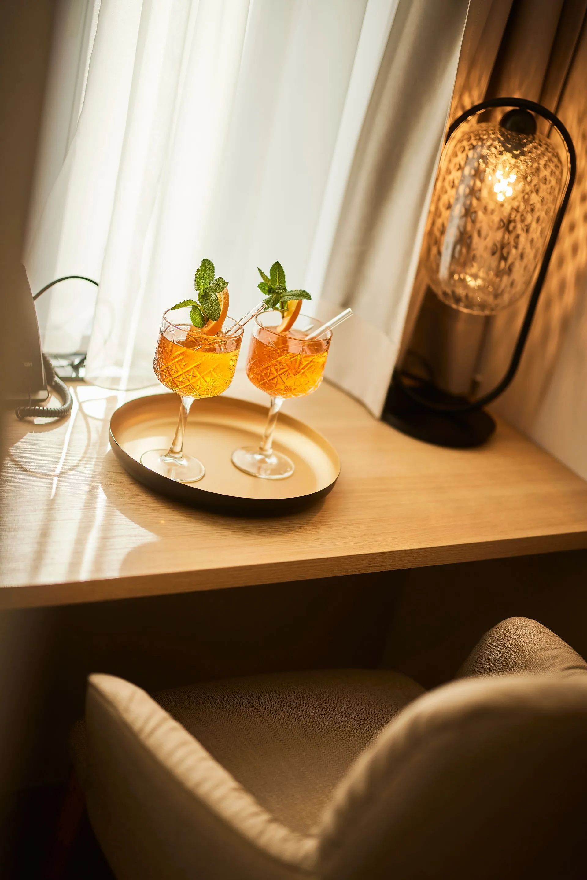 Zwei Cocktails auf einem Tablett, neben einer Lampe und einem Fenster, über einem Stuhl.