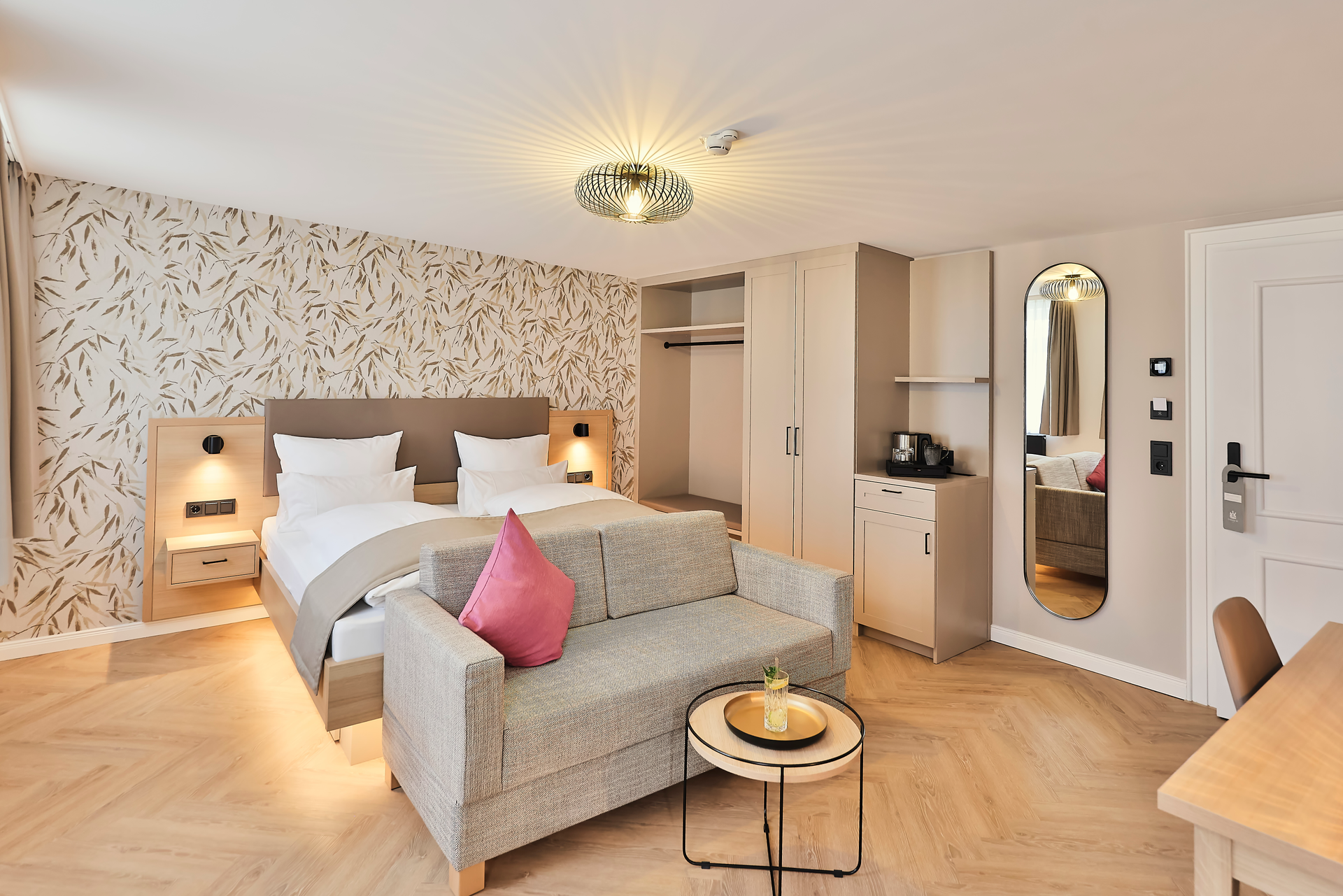 Hotelzimmer mit Doppelbett, Sofa, Kleiderschrank, Tisch. Helles, modernes Design, helle Holztöne.