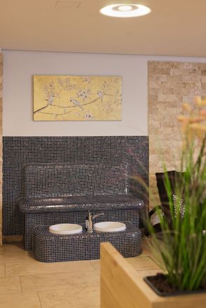 Spa-Fußbad mit schwarz-weißen Mosaikfliesen, hellbrauner Wand, goldener Kunst und Pflanze.