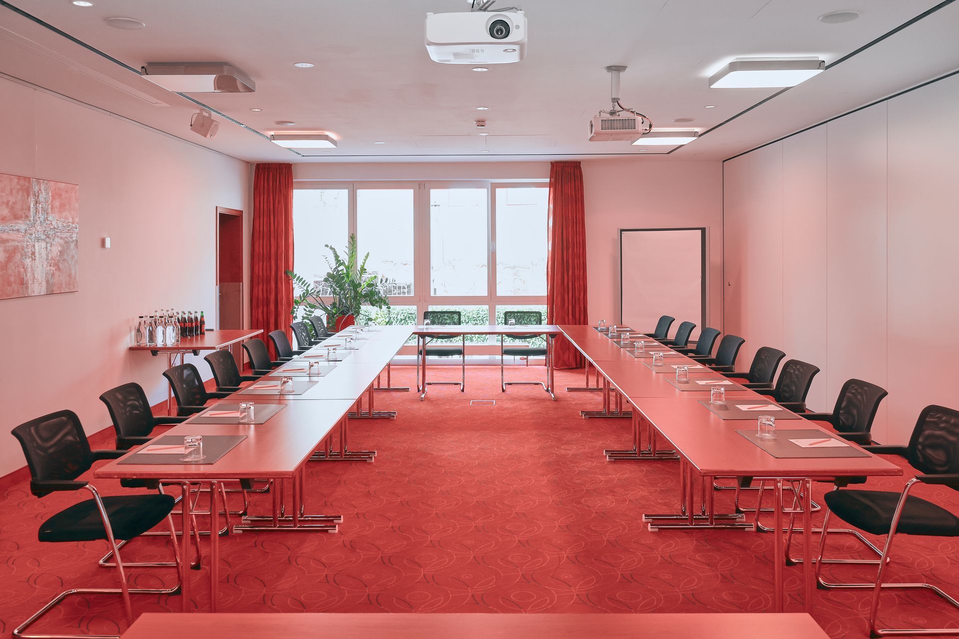 Konferenzraum mit zwei langen Tischen, schwarzen Stühlen, rotem Teppich und Fenster.
