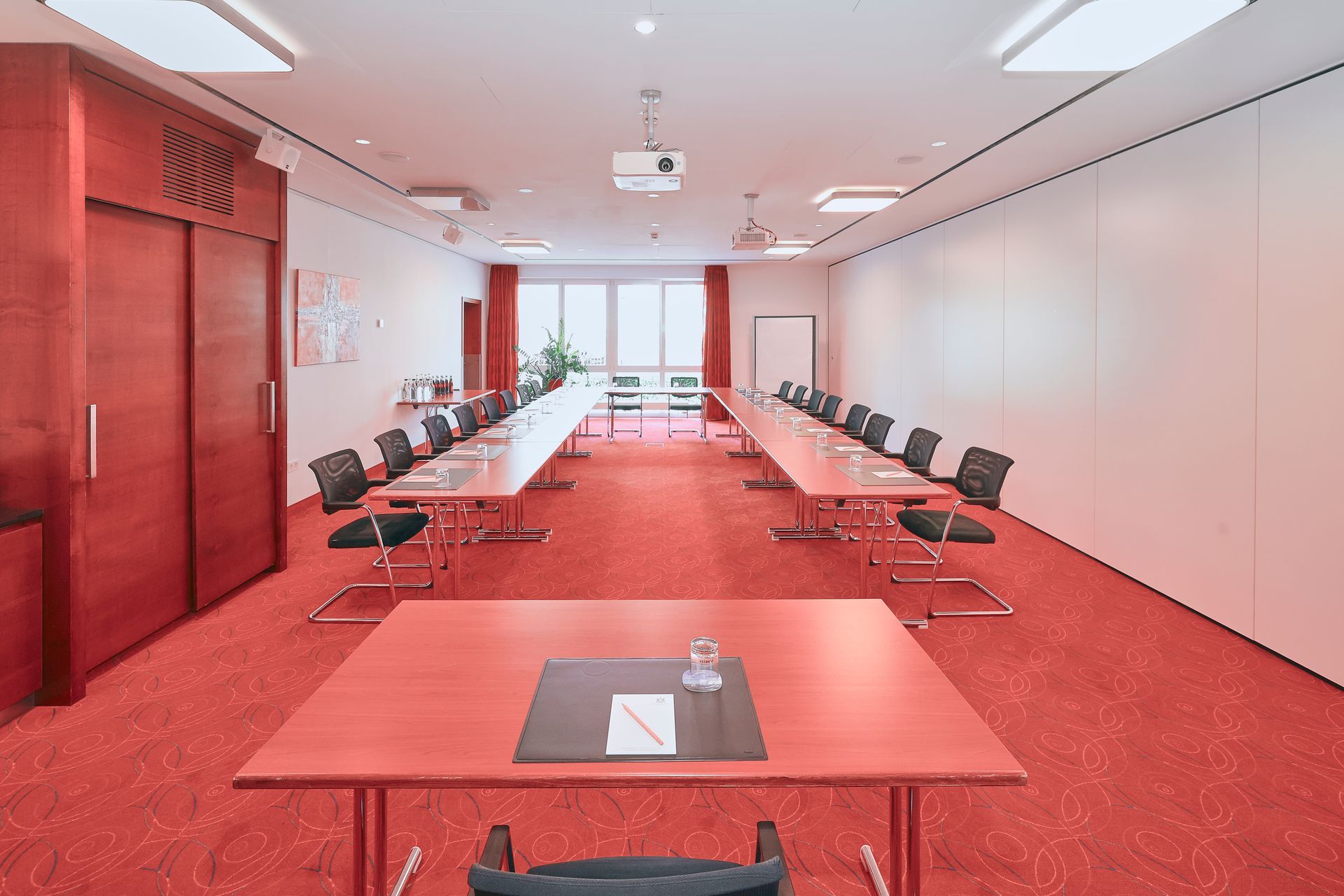Konferenzraum mit rotem Teppich, Tischen, Stühlen und Projektor.