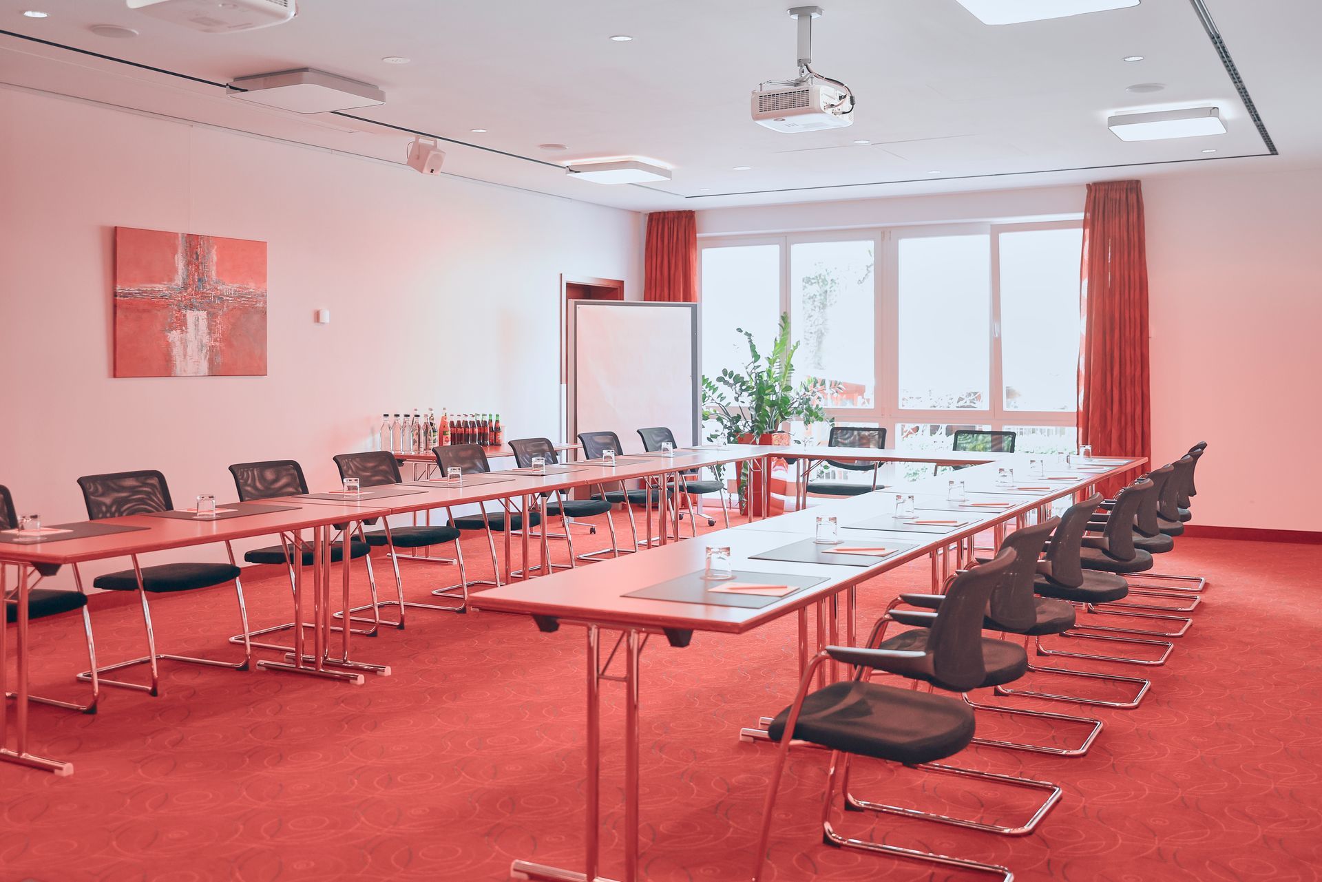 Konferenzraum mit rotem Teppich, langen Tischen, Stühlen und einem Whiteboard.