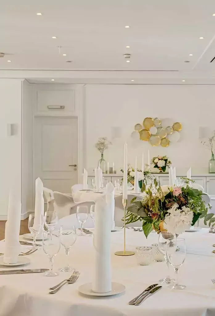 Elegant gedeckter Esstisch für eine formelle Veranstaltung; weiße Tischdecke, Gedecke, Blumenschmuck, Kerzen.