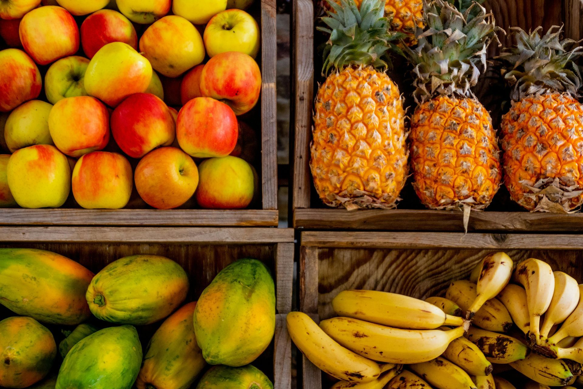 Äpfel, Ananas, Papayas und Bananen werden in Holzkisten präsentiert.
