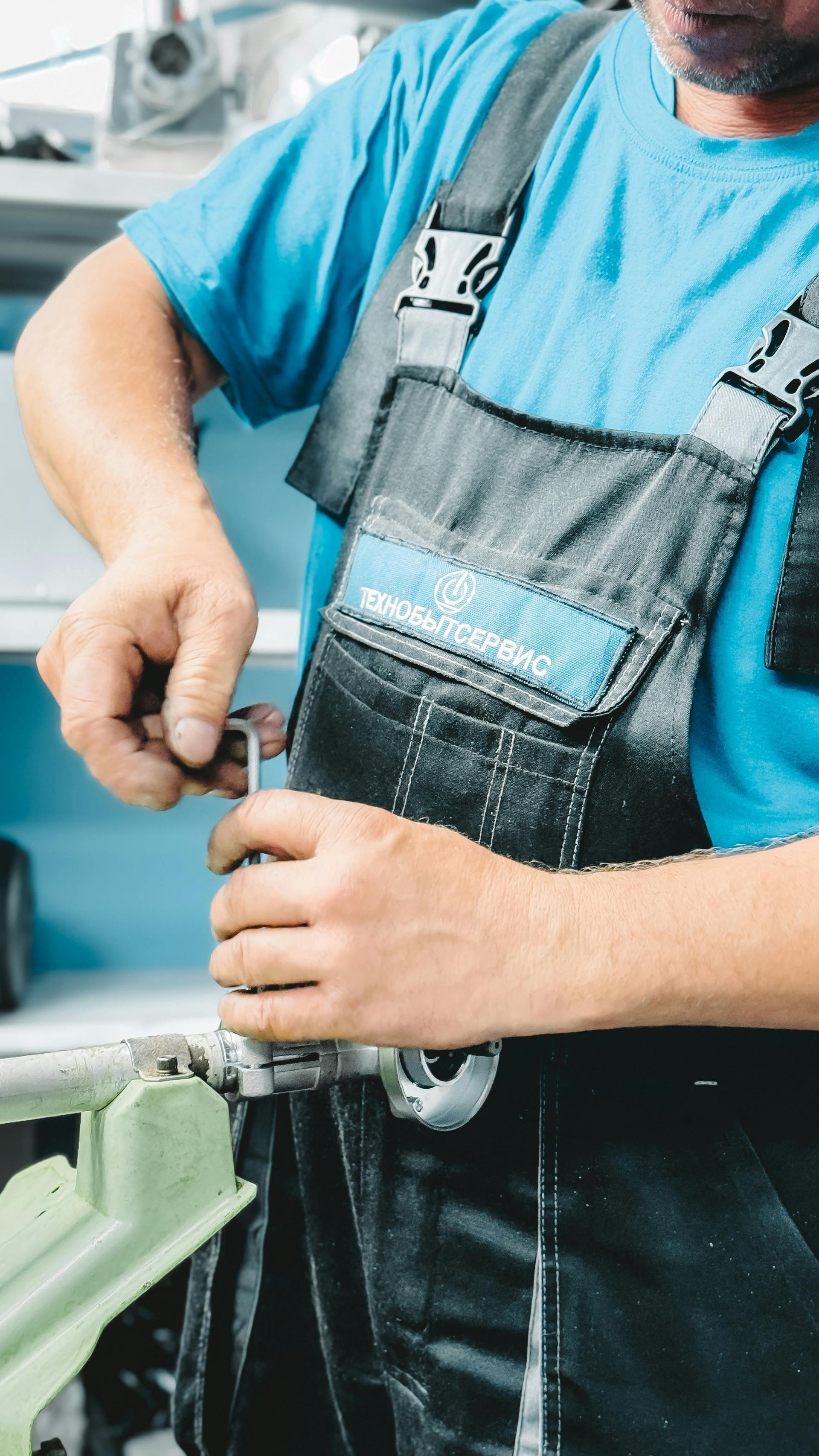 Mann in blauem Hemd und Overall arbeitet mit einem Schraubenschlüssel an Maschinen.