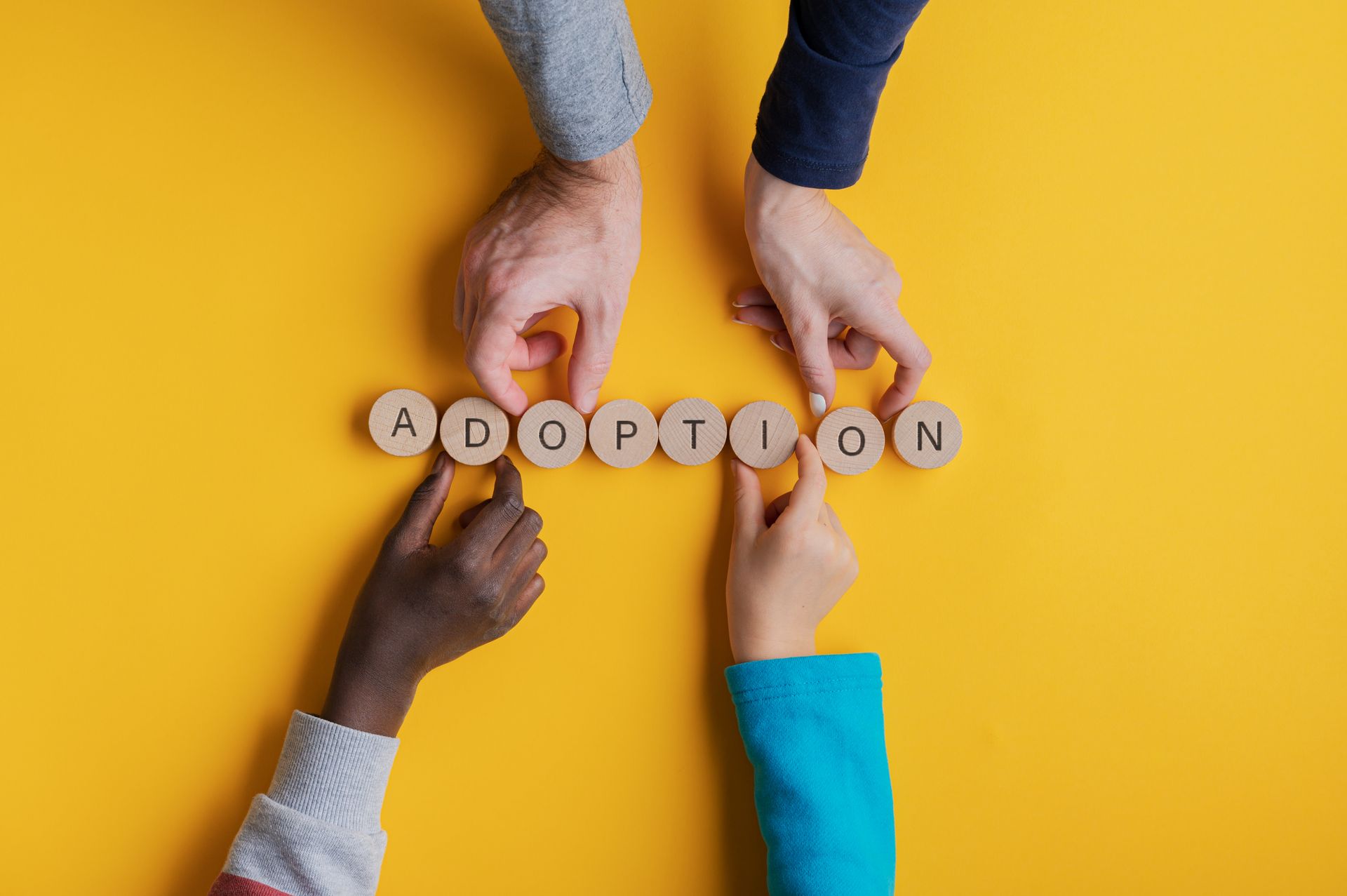 Quatre mains et des lettres formant le mot adoption