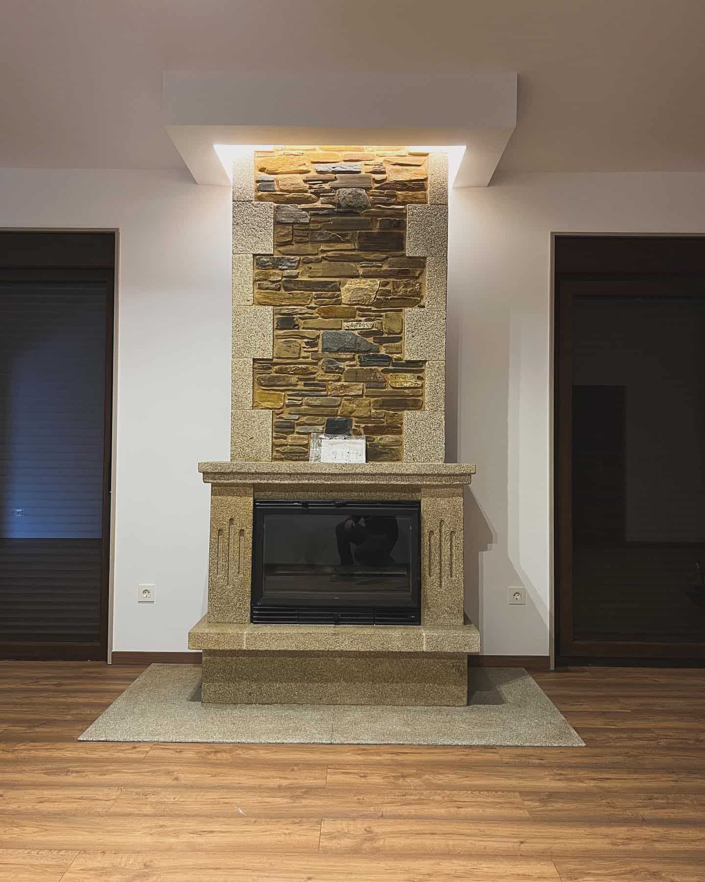 Chimenea con piedra apilada y marco de granito, iluminación empotrada y caja de fuego de vidrio negro.