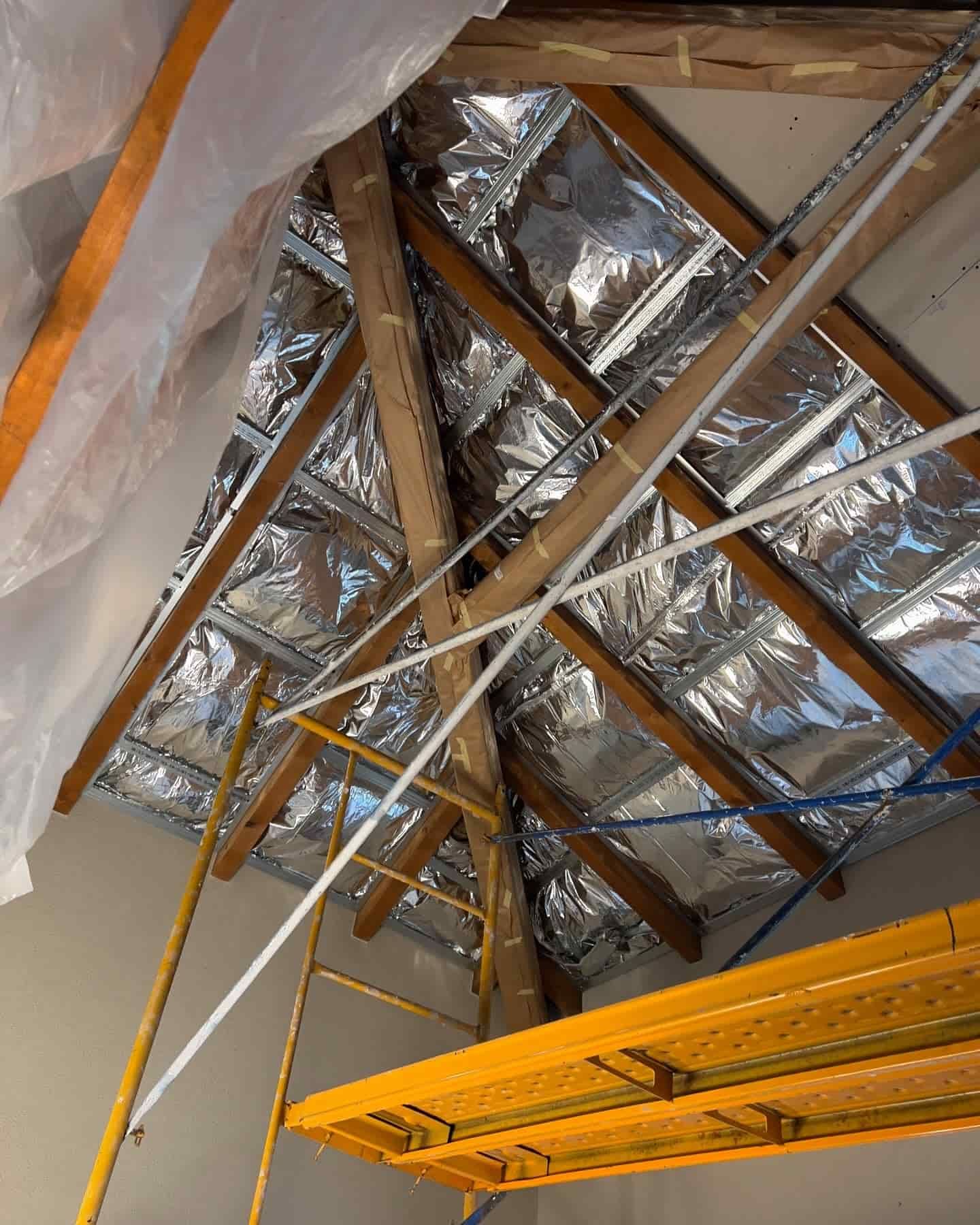 Ático con vigas de madera vistas, aislamiento reflectante y andamios.