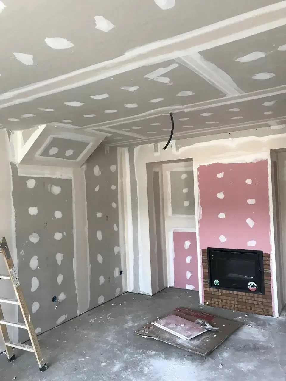 Interior en construcción con paneles de yeso y chimenea sin terminar.