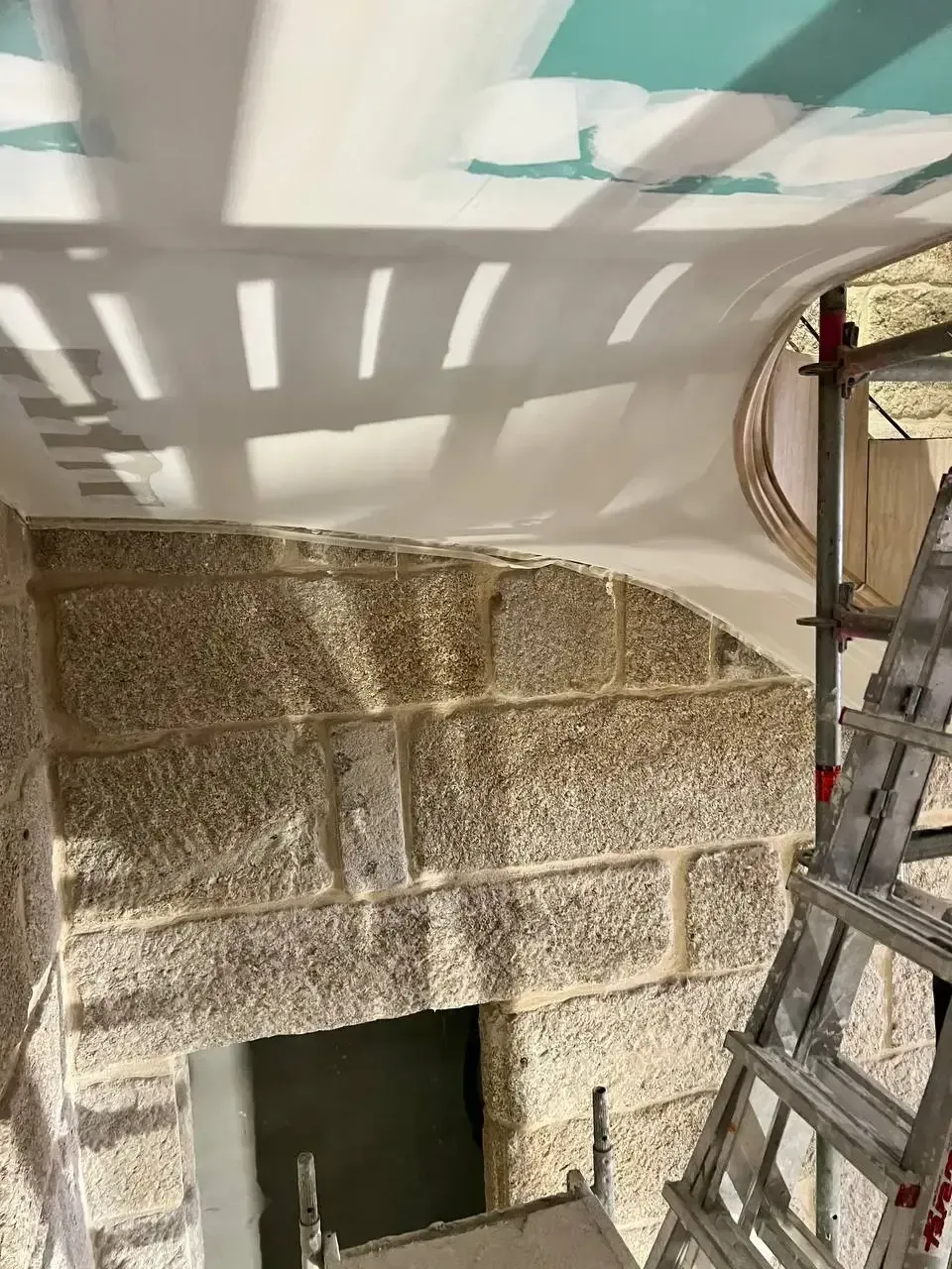 Puerta de piedra en construcción con techo de yeso blanco y andamios.