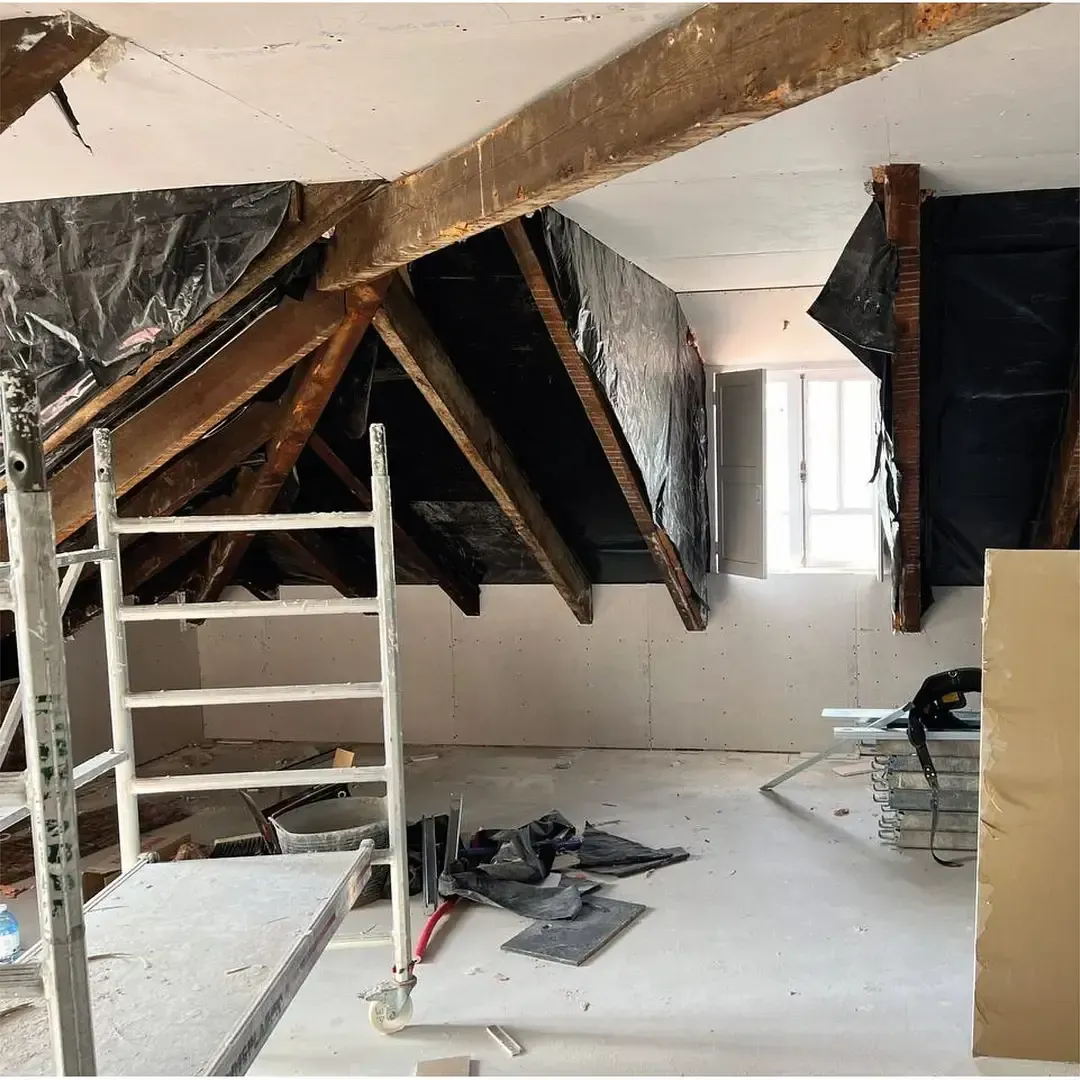 Renovación del espacio interior del ático en progreso; vigas expuestas, paredes y escalera visibles.