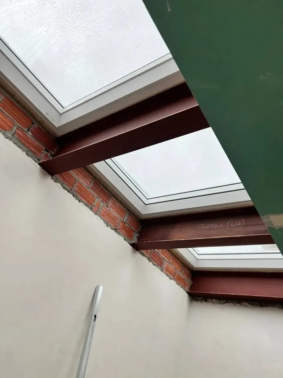 Vista interior de tragaluces, ladrillo rojo y vigas de acero marrones. Paredes claras y soporte verde.