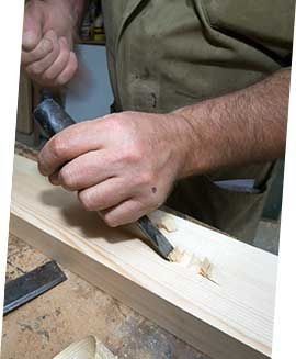 Persona que utiliza un cincel para tallar madera en un banco de trabajo.