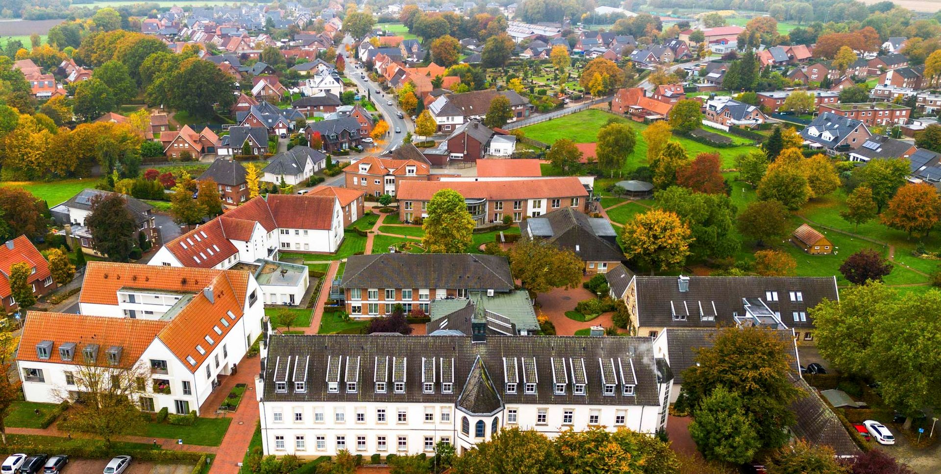 Frau im Rollstuhl mit Pflegekraft in einem grünen Garten. Die Pflegekraft lächelt und berührt die Schulter der Frau.