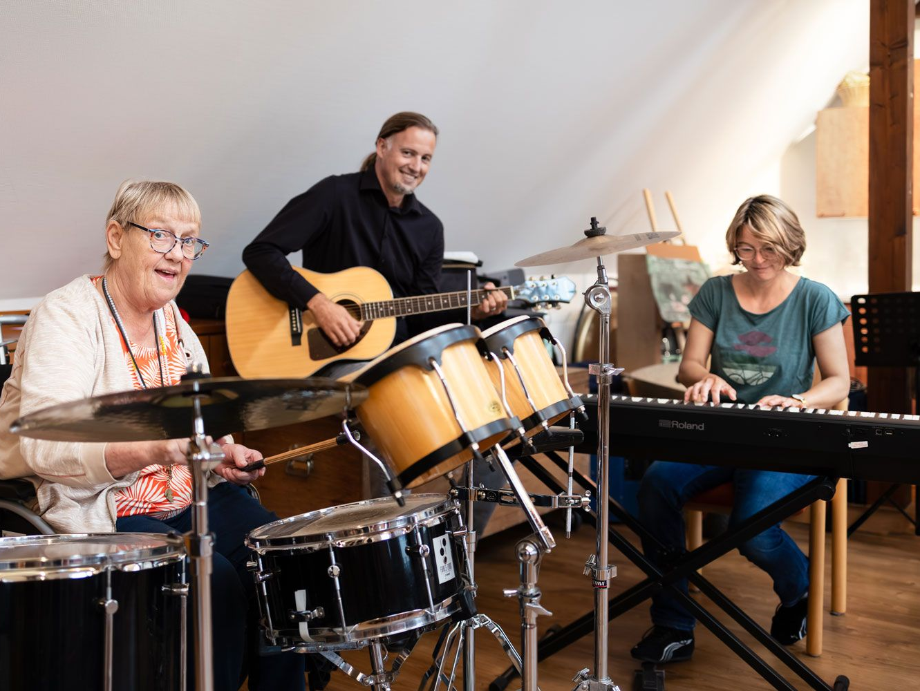 Drei Männer auf einer Wiese mit einem Fußball. Einer kickt den Ball, zwei schauen zu. Grüner Torpfosten links.