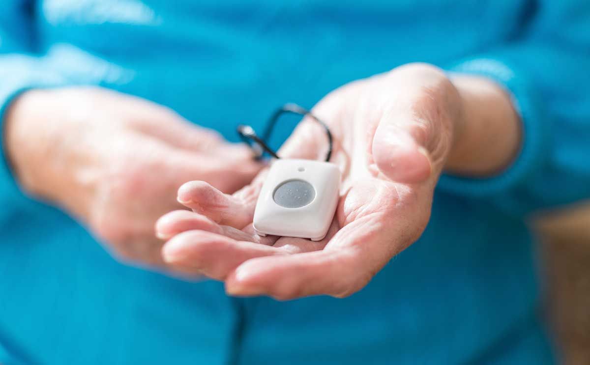 Ältere Hände halten einen weißen Notrufknopf mit schwarzer Kordel.