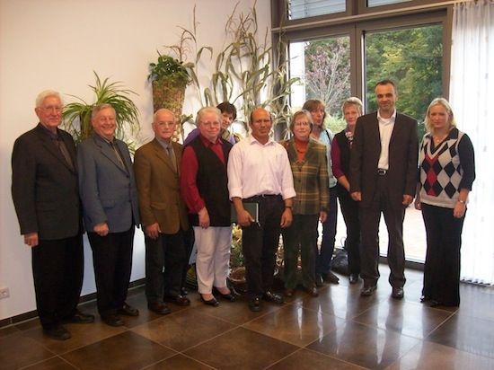 Gruppe von Menschen, die in einem Innenbereich stehen; wahrscheinlich eine formelle Versammlung oder ein Porträt.