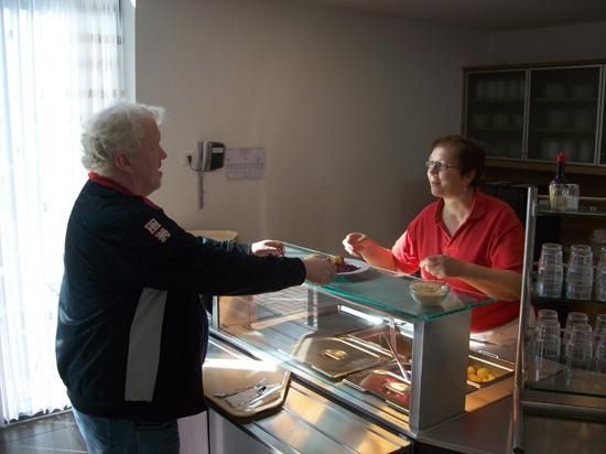 Ein Mann kauft in einer hell erleuchteten Umgebung Essen von einer Frau hinter einer Essenstheke.