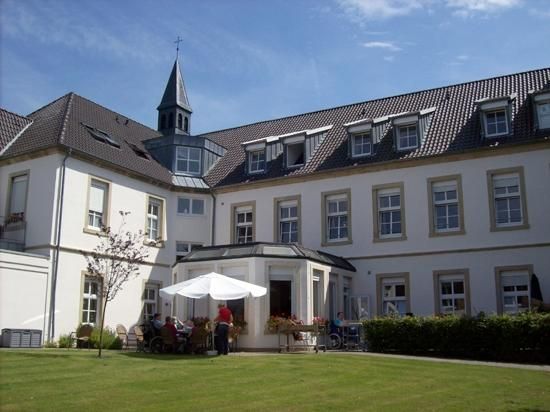 Weißes Gebäude mit Turm, Fenstern und Sitzbereich im Freien auf einer Rasenfläche unter einem sonnigen blauen Himmel.