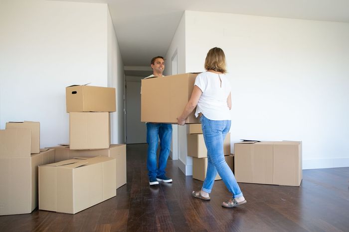 Un hombre y una mujer llevan cajas en una habitación vacía.