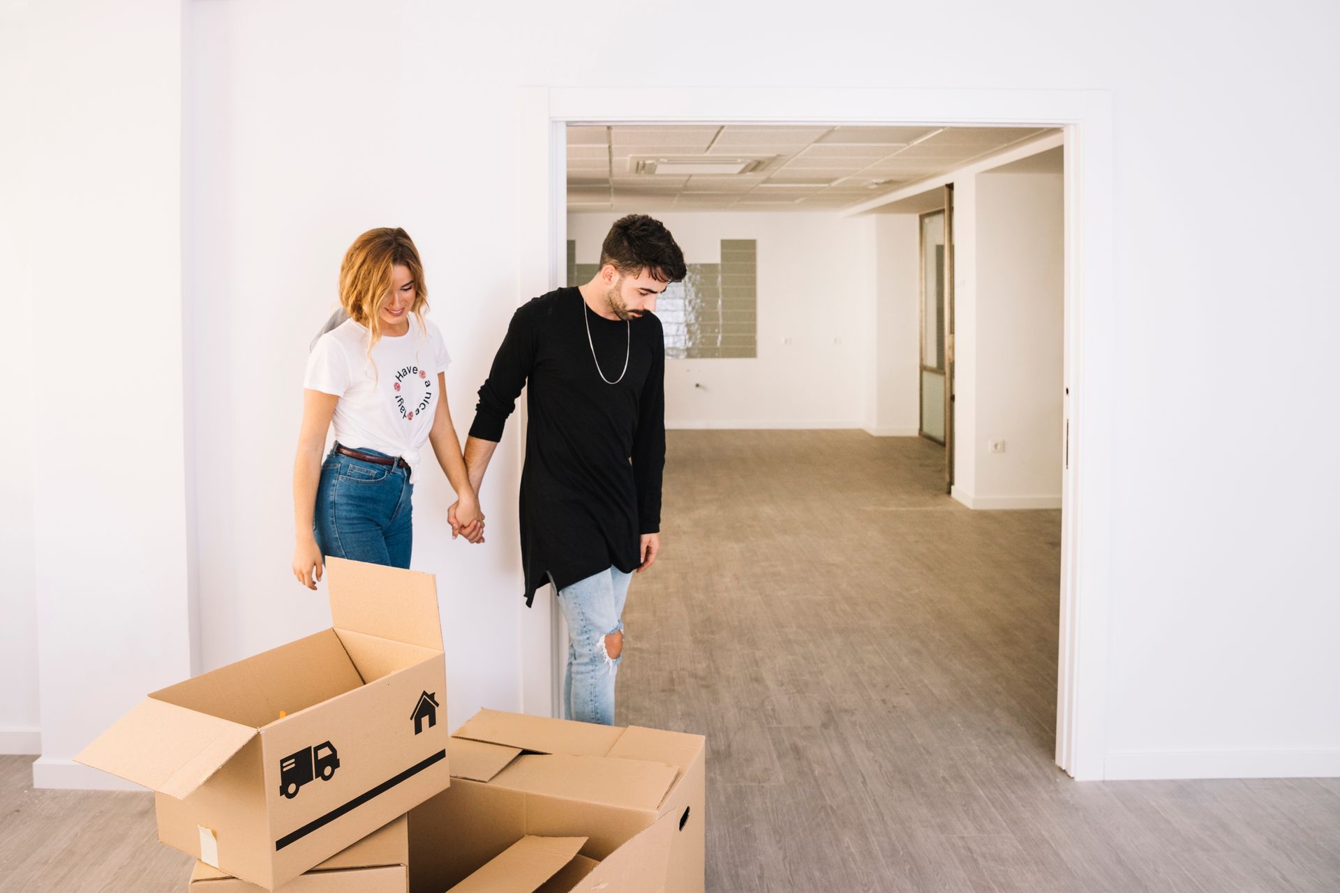 Un hombre y una mujer se toman de la mano en una habitación vacía con cajas de cartón.