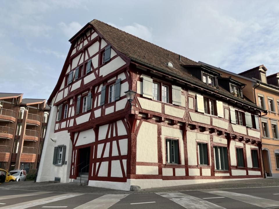Fachwerkbau mit roten Balken und weisser Ausfachung, drei Stockwerke und Satteldach.