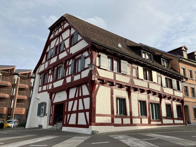 Fachwerkbau mit roten Balken und weisser Ausfachung, drei Stockwerke und Satteldach.