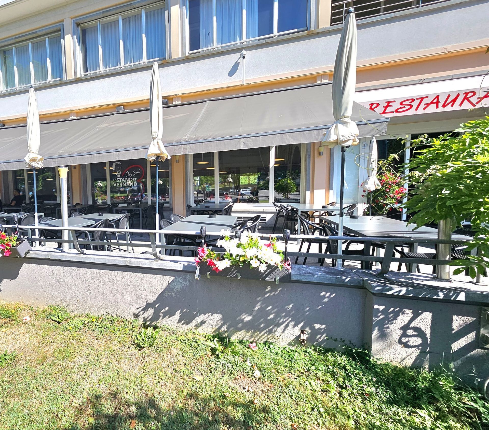 Extérieur du restaurant Le Stand de Vernand avec sièges extérieurs, auvents et jardinières.