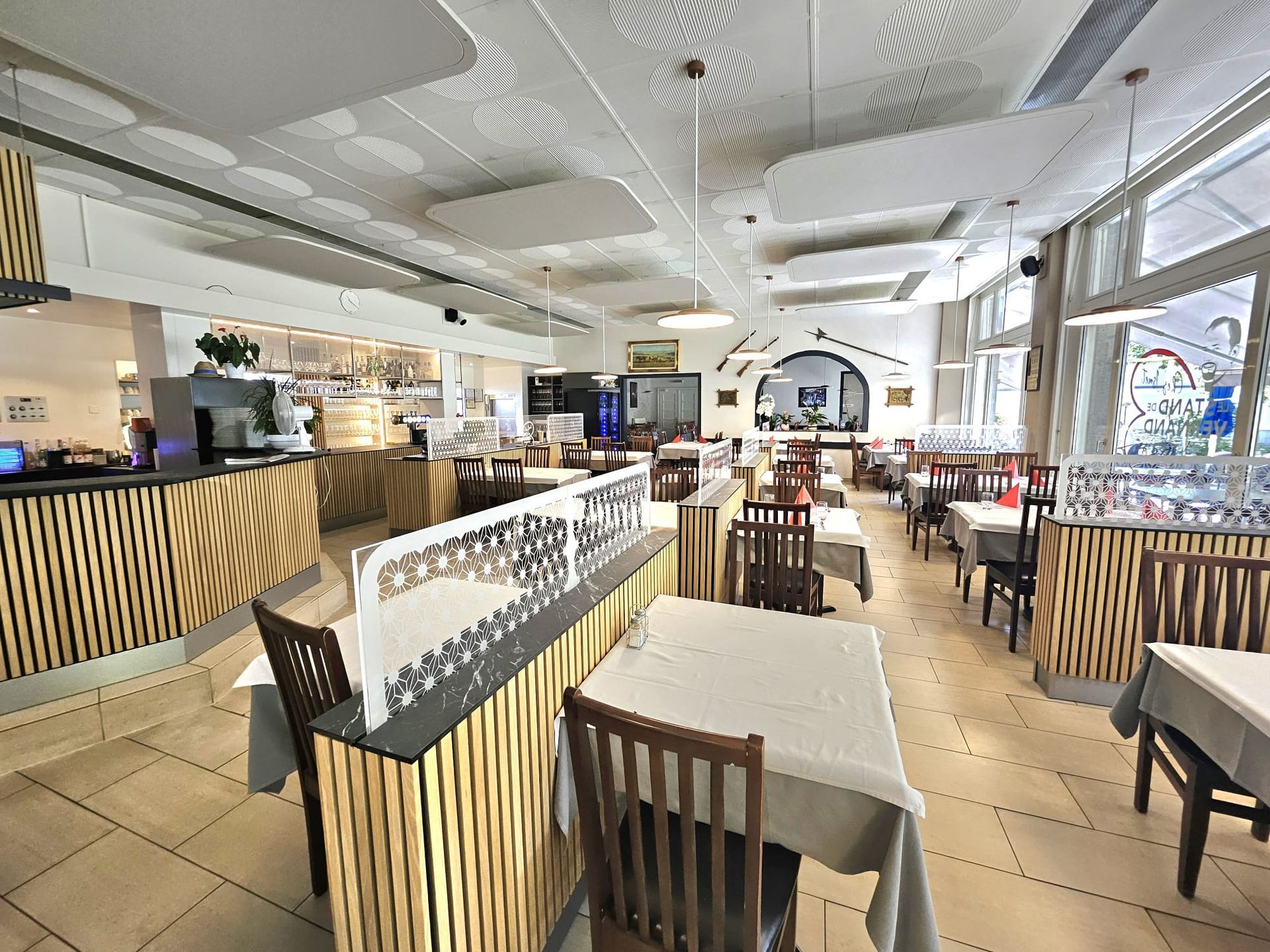 Intérieur du restaurant avec tables, chaises et bar. La lumière du soleil entre par les fenêtres.