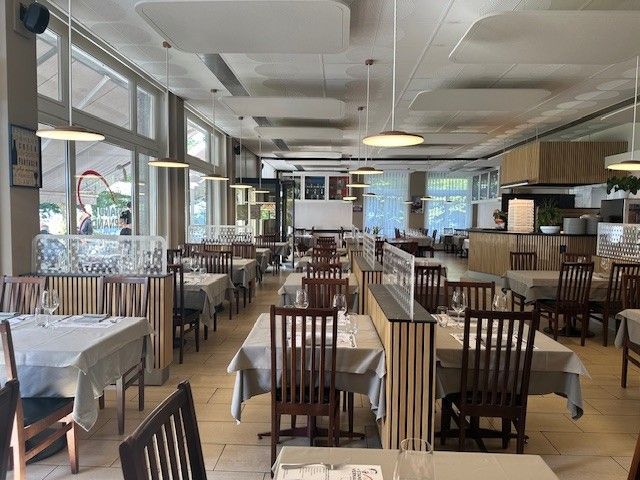 Intérieur de restaurant avec des tables dressées pour dîner, des nappes, des chaises en bois et de grandes fenêtres.
