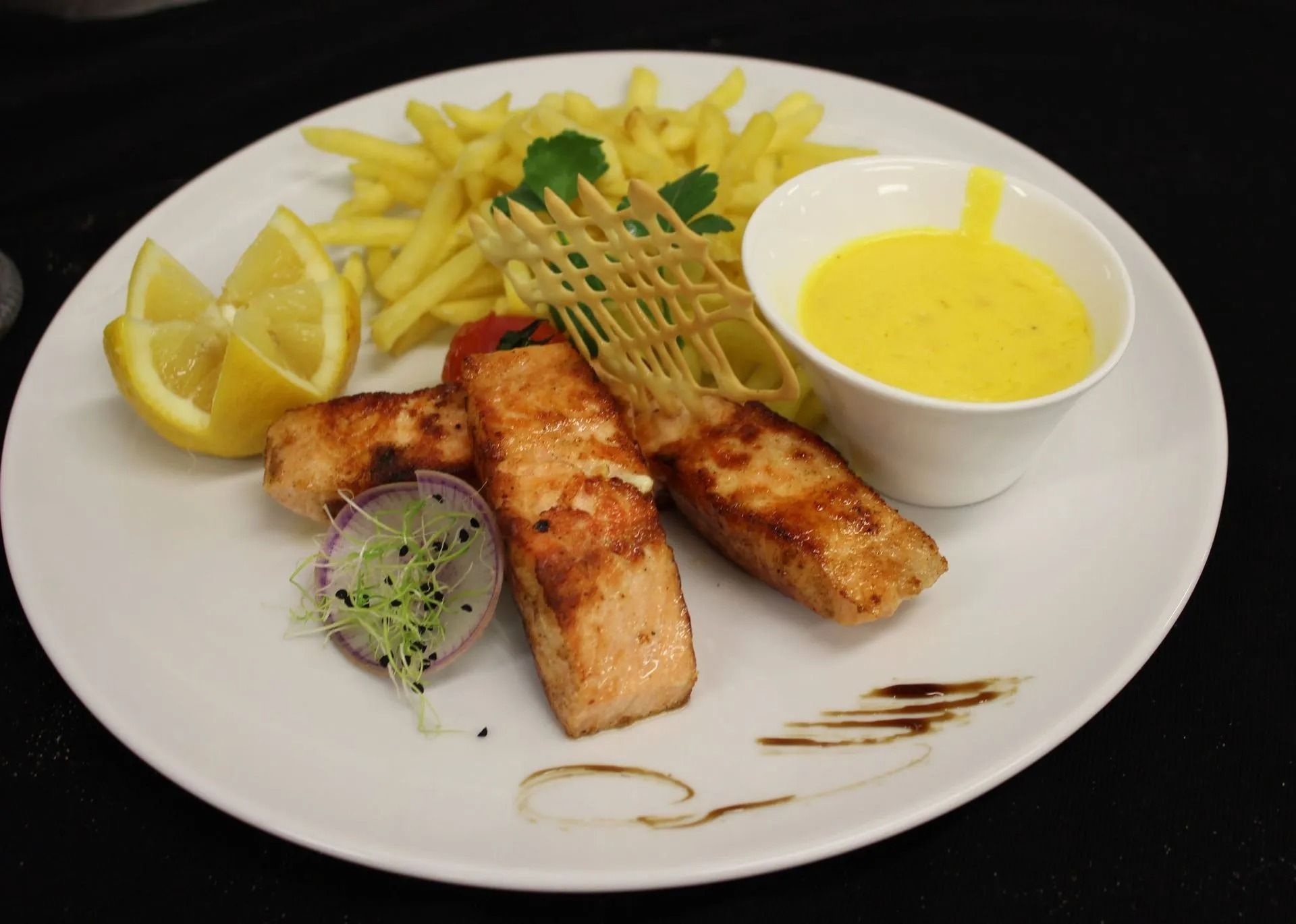 Saumon grillé avec frites, sauce, citron et garniture sur une assiette blanche.