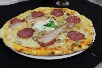 Une pizza avec du jambon, du salami et un œuf sur une assiette blanche sur une table.