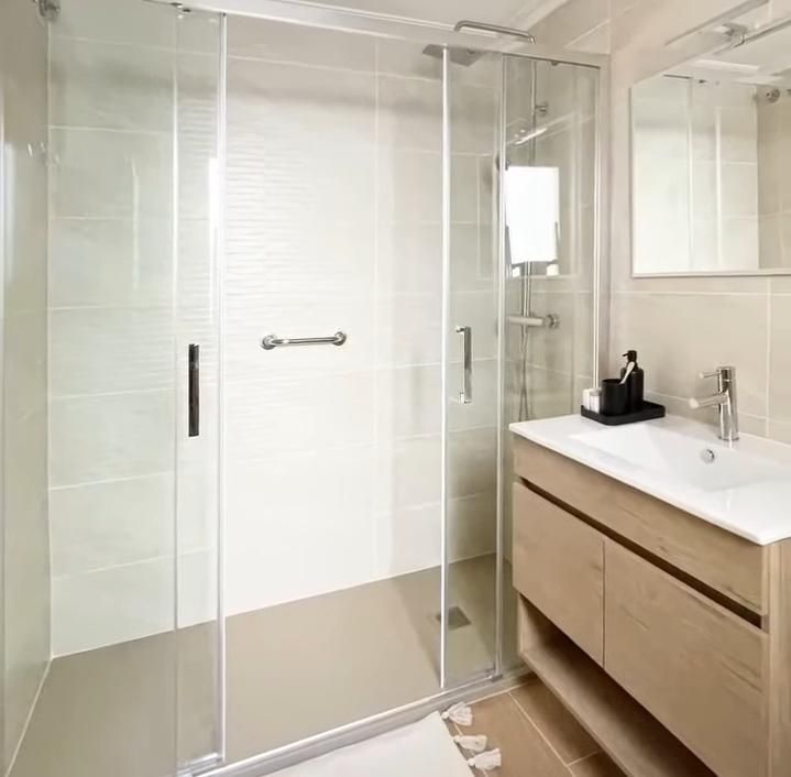 Un baño moderno con una ducha a ras de suelo con mampara de cristal y barra de apoyo, junto a un tocador de madera
