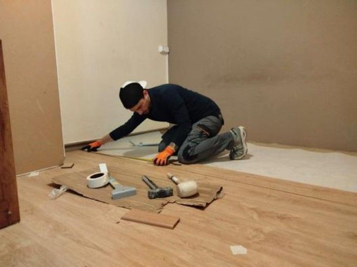 Una persona se arrodilla en el suelo y utiliza una cinta métrica para instalar un suelo de madera en una habitación