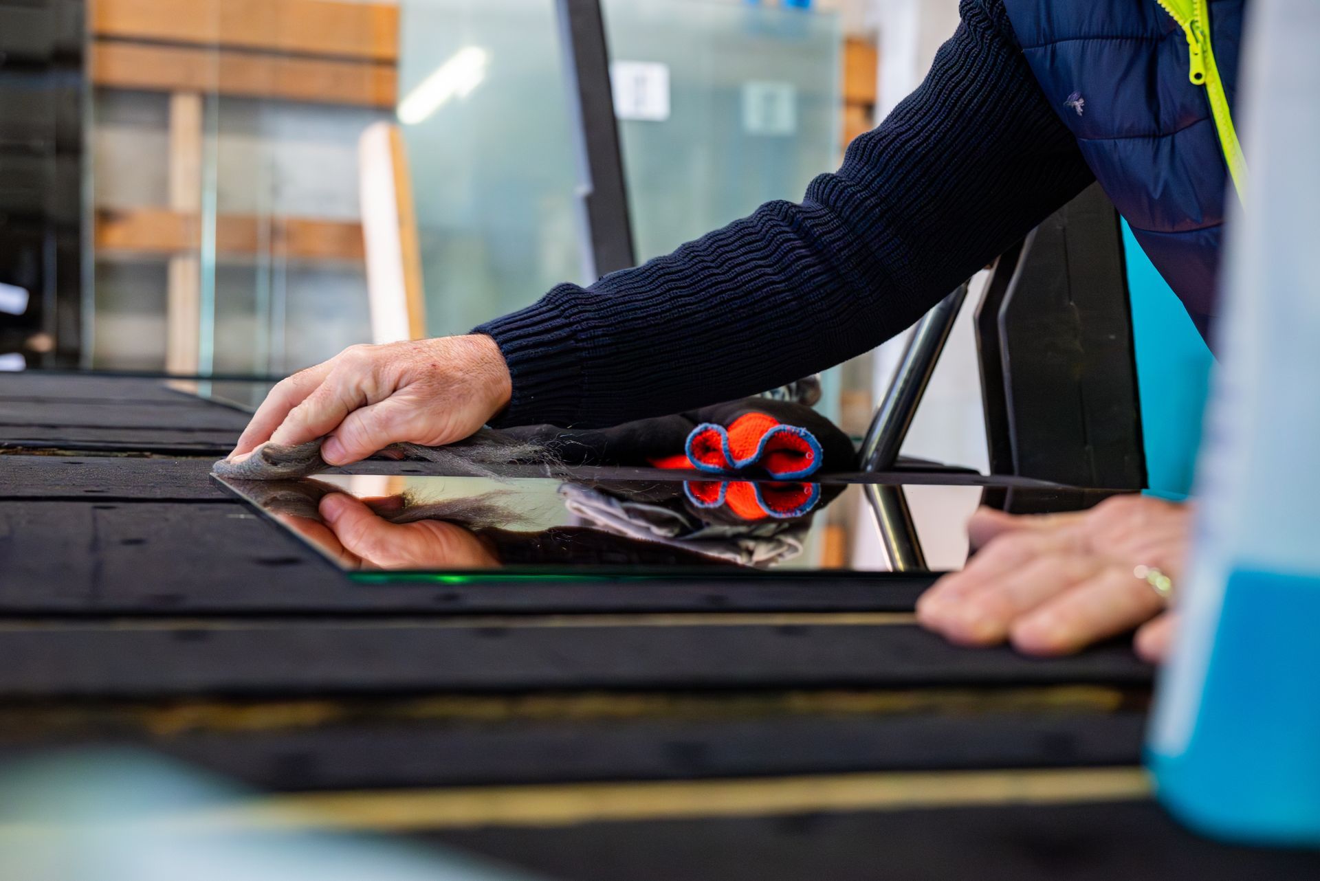 Dans un atelier, une personne utilise un chiffon pour essuyer une vitre sur un établi sombre.