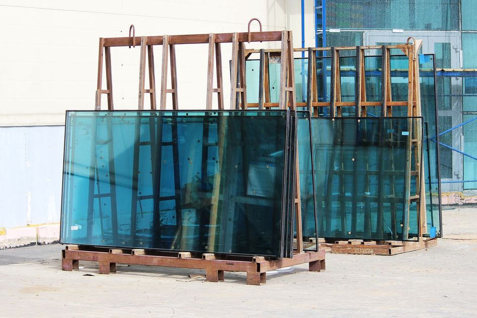 De grandes piles de plaques de verre architectural teintées en bleu sont stockées à l'extérieur sur des palettes, dans des rayonnages métalliques en forme de A.