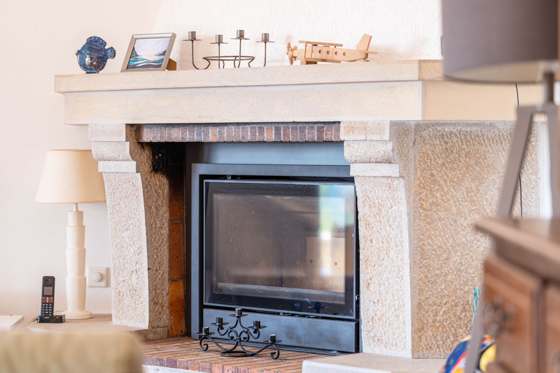 Une cheminée en pierre sur laquelle sont posés un cadre photo, des bougeoirs et une petite maquette d'avion en bois.