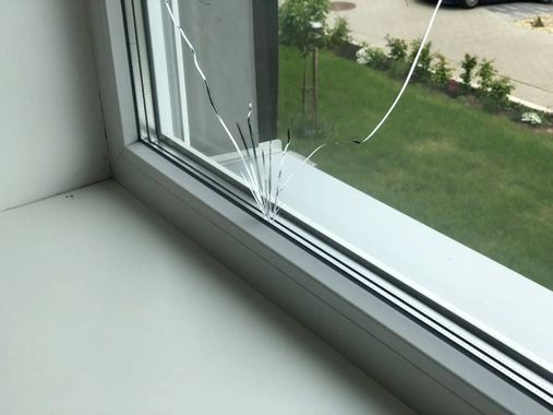 Eine Person bringt selbstklebende Fensterisolationsstreifen an einem weissen Rahmen an, während eine Dichtmittelpistole in der Nähe auf der Fensterbank liegt.