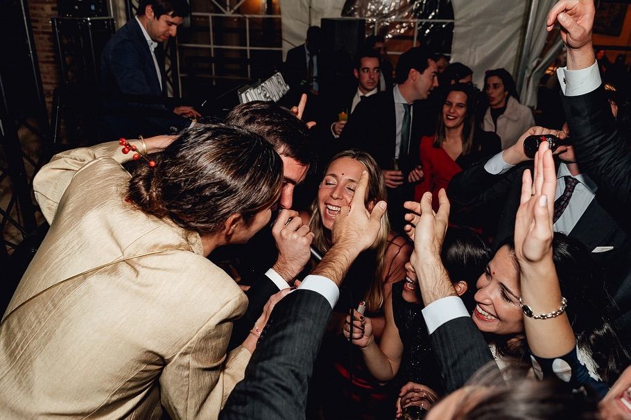 Gente riendo y bailando en una animada fiesta en interiores, con las manos en alto y sonrisas en el rostro.