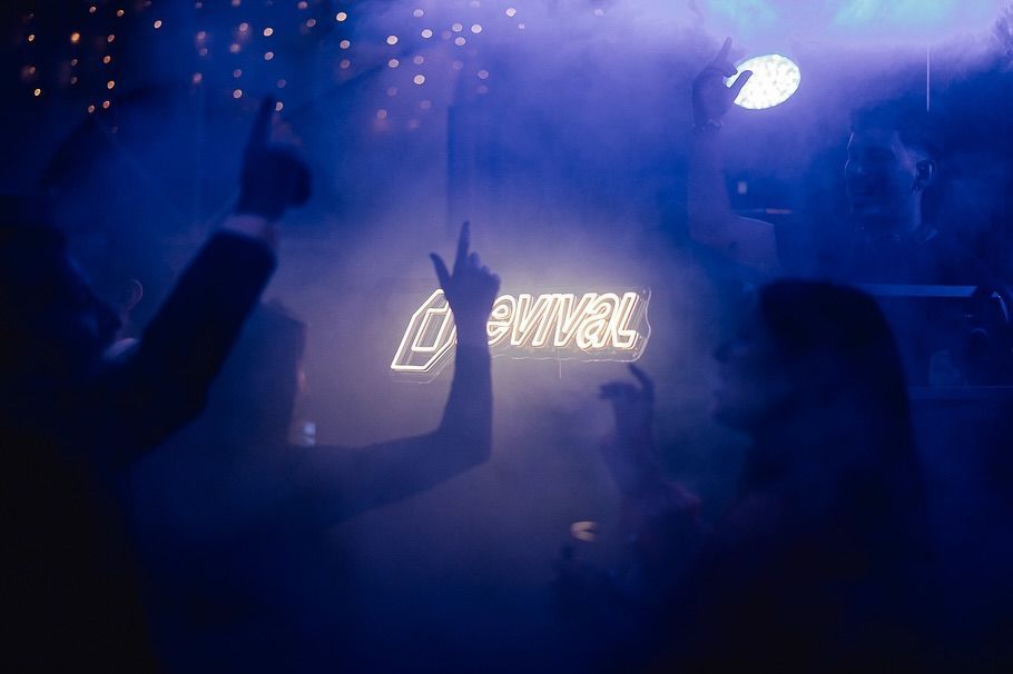 Multitud bailando bajo la iluminación azul de un concierto, con las manos en alto y un letrero luminoso en el escenario
