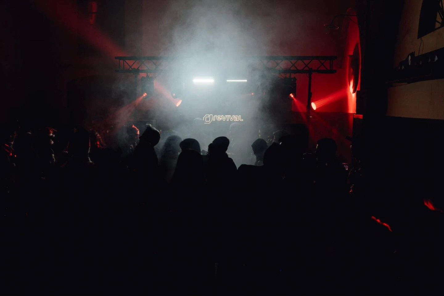 Siluetas del público de cara a un escenario iluminado y lleno de humo, con luces rojas, en un concierto