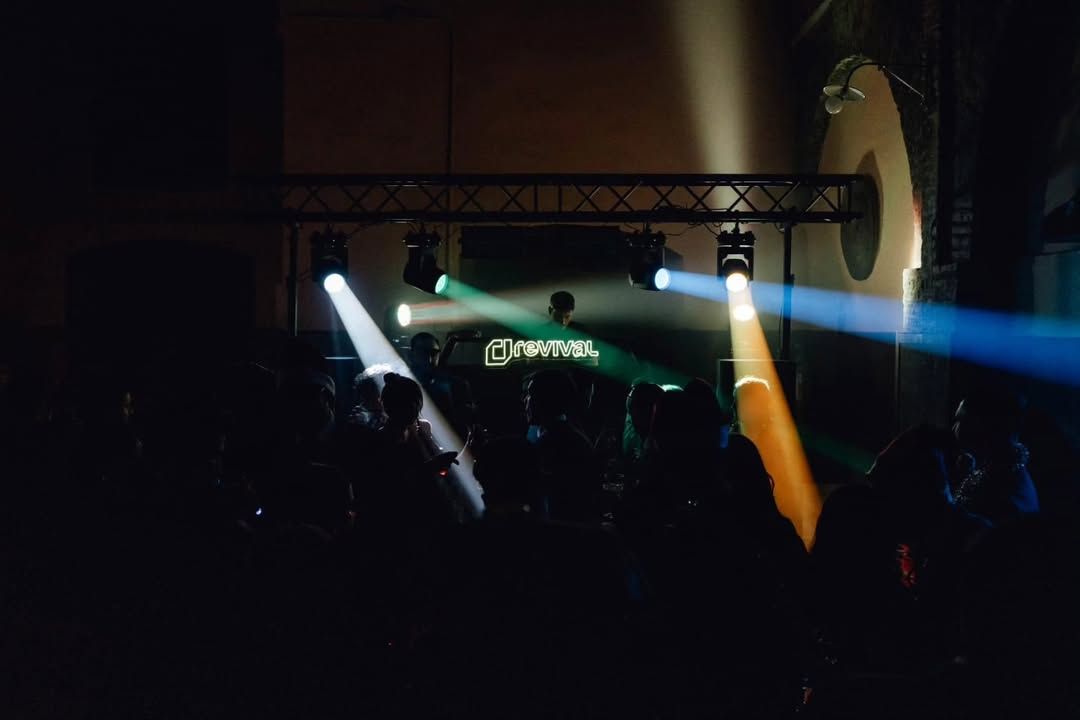 Escenario de concierto con focos blancos, verdes y azules que iluminan a un público en penumbra