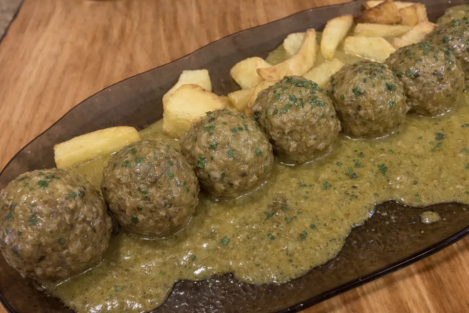 Albóndigas en salsa verde con patatas fritas en bandeja.