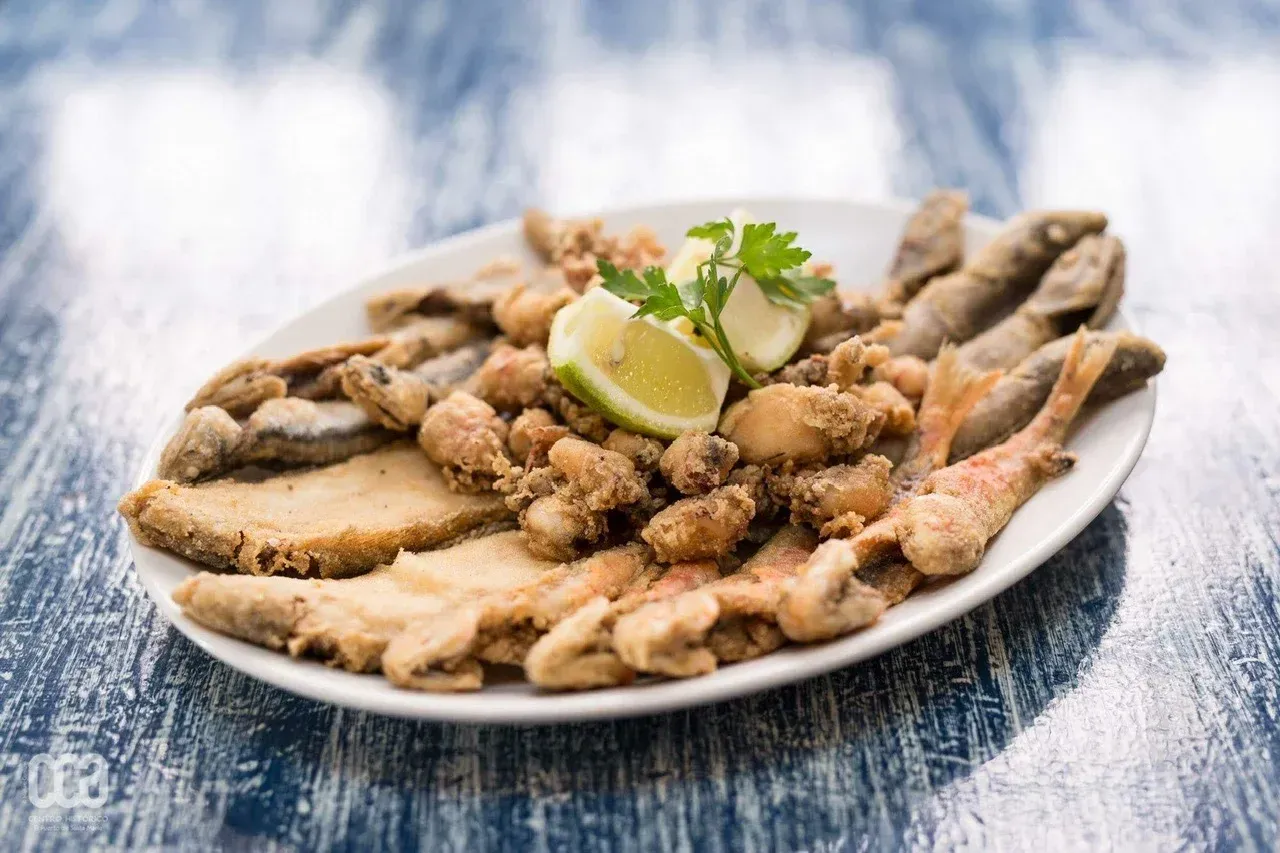 Plato de mariscos fritos, incluido pescado, con guarnición de limón y perejil sobre una mesa de madera azul.