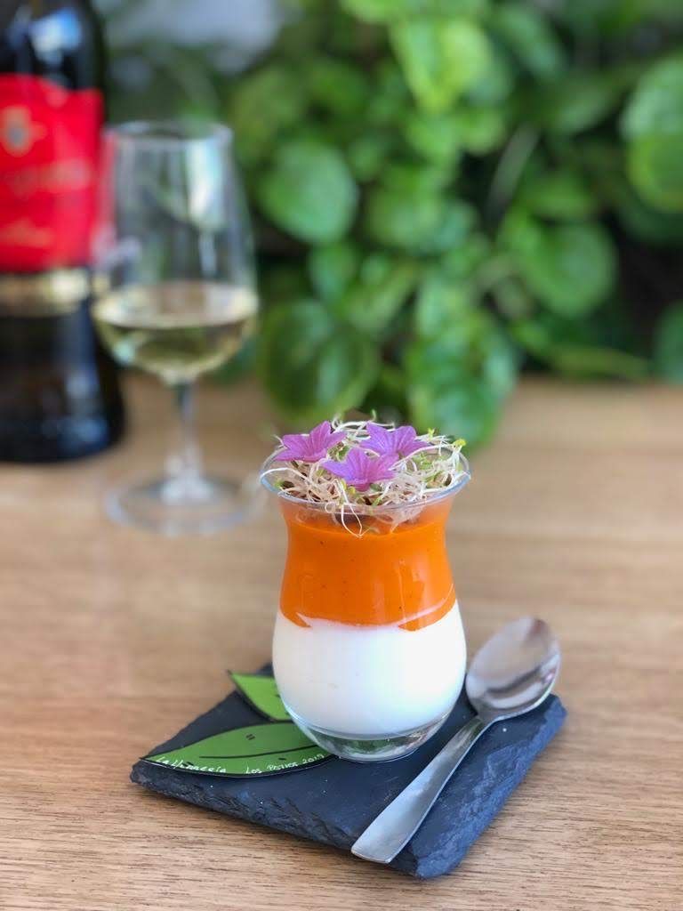 Postre en capas de color naranja y blanco, cubierto con brotes y flores,