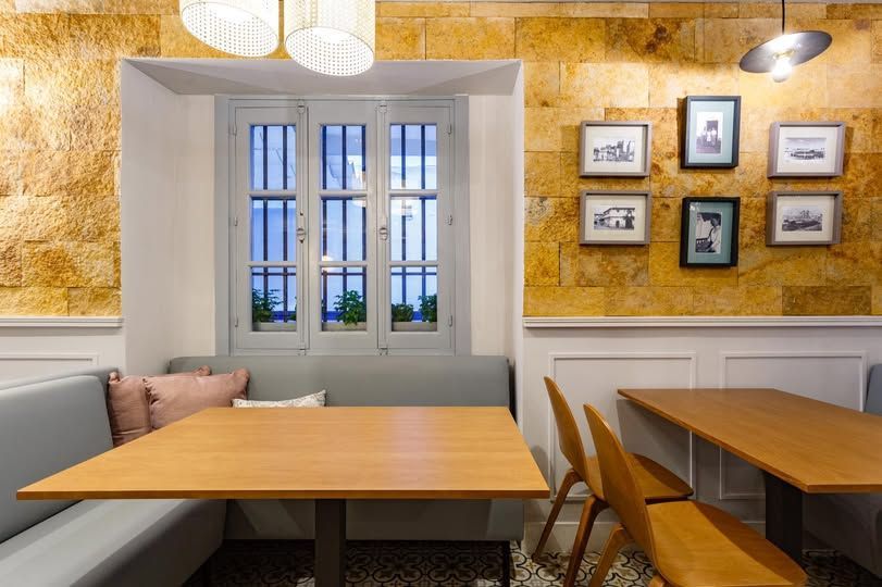 Interior de restaurante con mesas de madera, bancos, pared de piedra y fotografías enmarcadas.