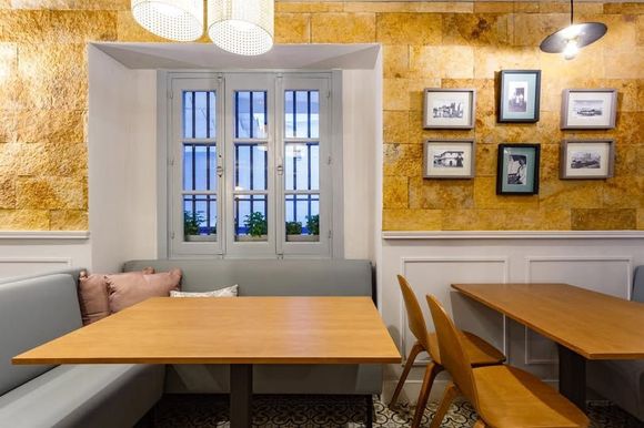 Interior de restaurante con mesas de madera, bancos, pared de piedra y fotografías enmarcadas.